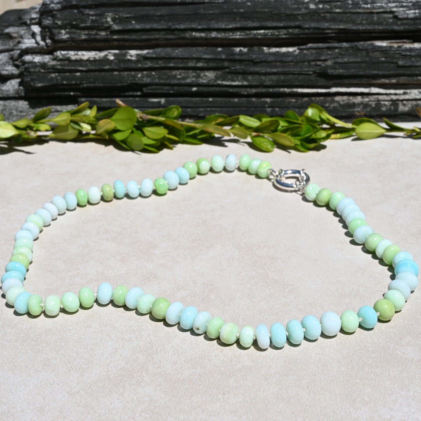 A beaded necklace made of pastel light blue, mint green, and pale yellow-green round beads, with a silver clasp. 