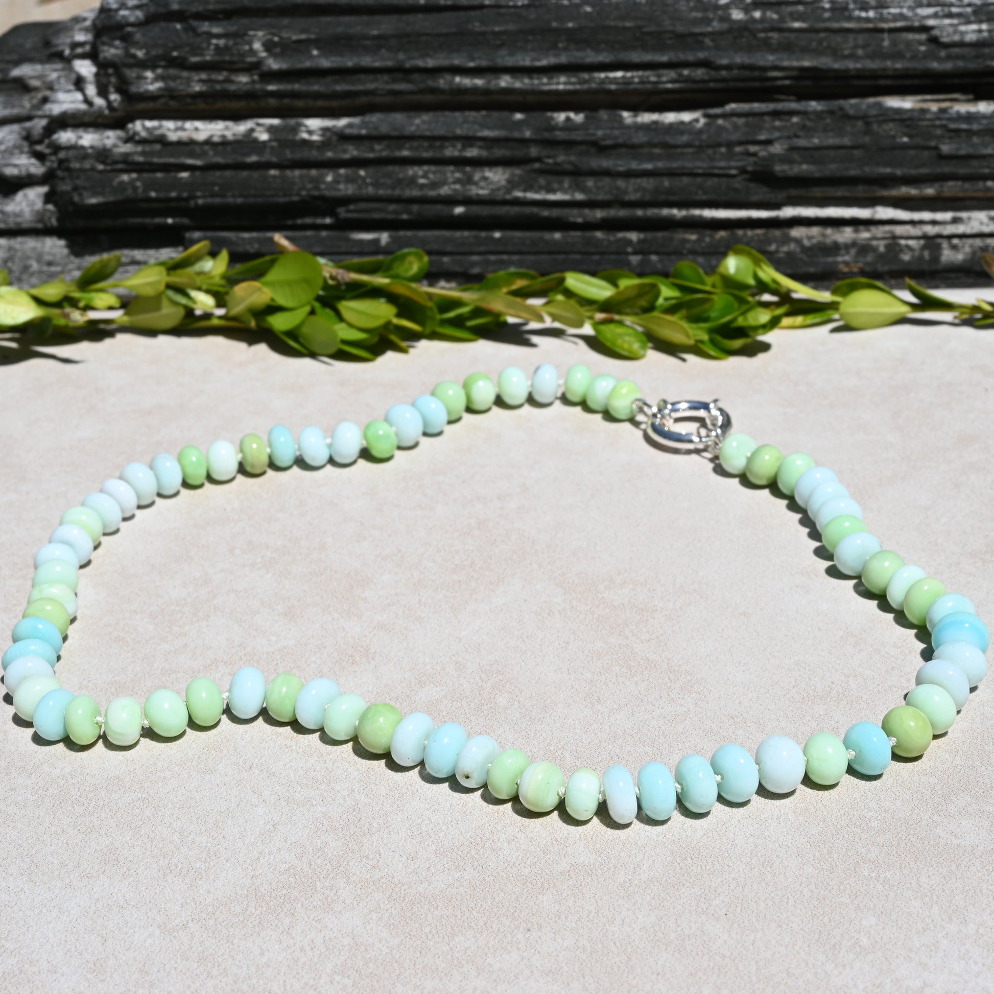 A beaded necklace made of pastel light blue, mint green, and pale yellow-green round beads, with a silver clasp. 