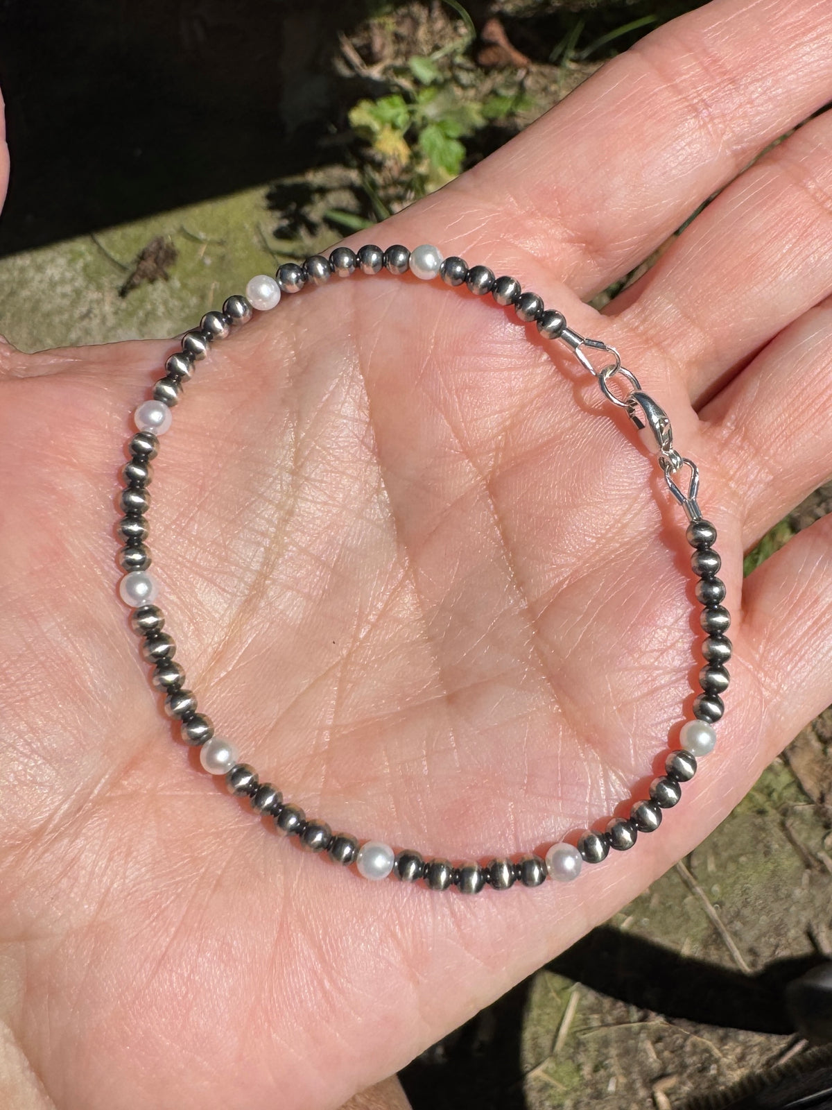 A beaded bracelet with dark metallic beads and small white pearls, shown resting on an open hand outdoors.